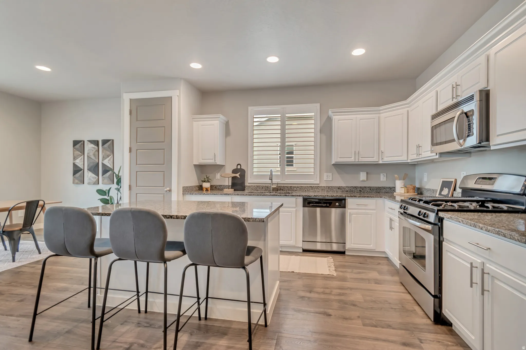 Kitchen featuring a center island with bar seating, granite countertops, white cabinetry, stainless steel appliances, and wood-finish flooring