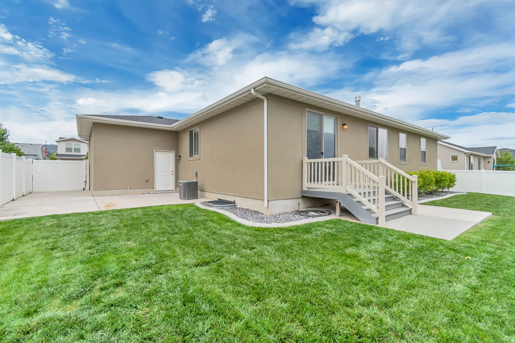 Expansive green lawn surrounds a stucco exterior with a concrete patio
