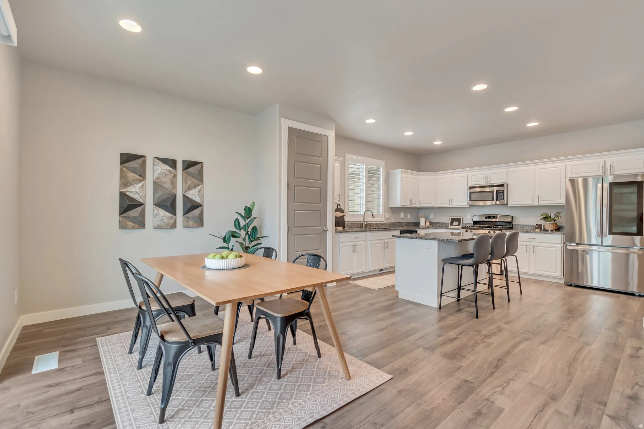 Open-concept kitchen and dining area featuring wood-finish flooring, white cabinetry, stainless steel appliances, and recessed lighting