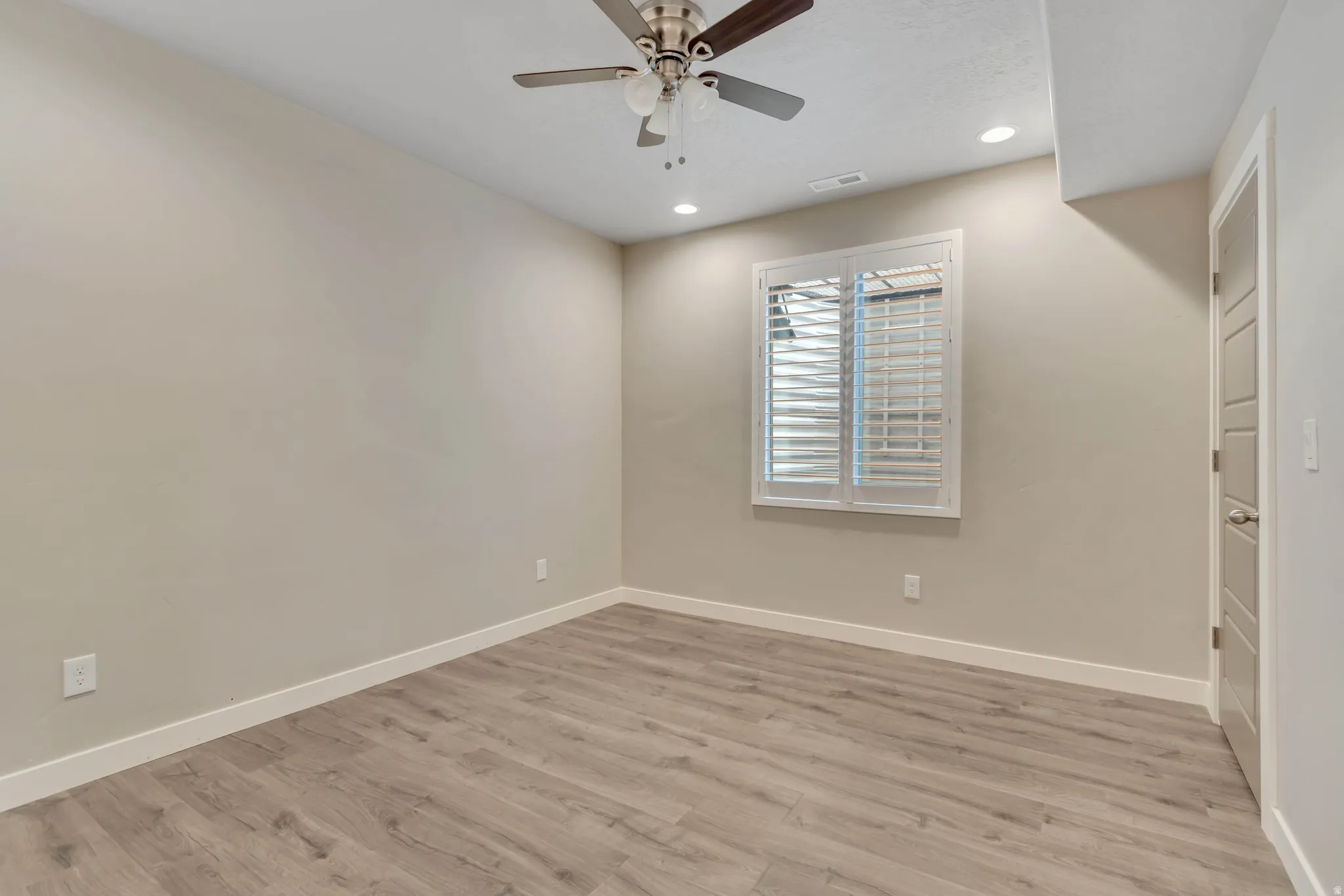 Interior room featuring wood-finish flooring, white baseboards, a window with plantation shutters, a ceiling fan, and recessed lighting