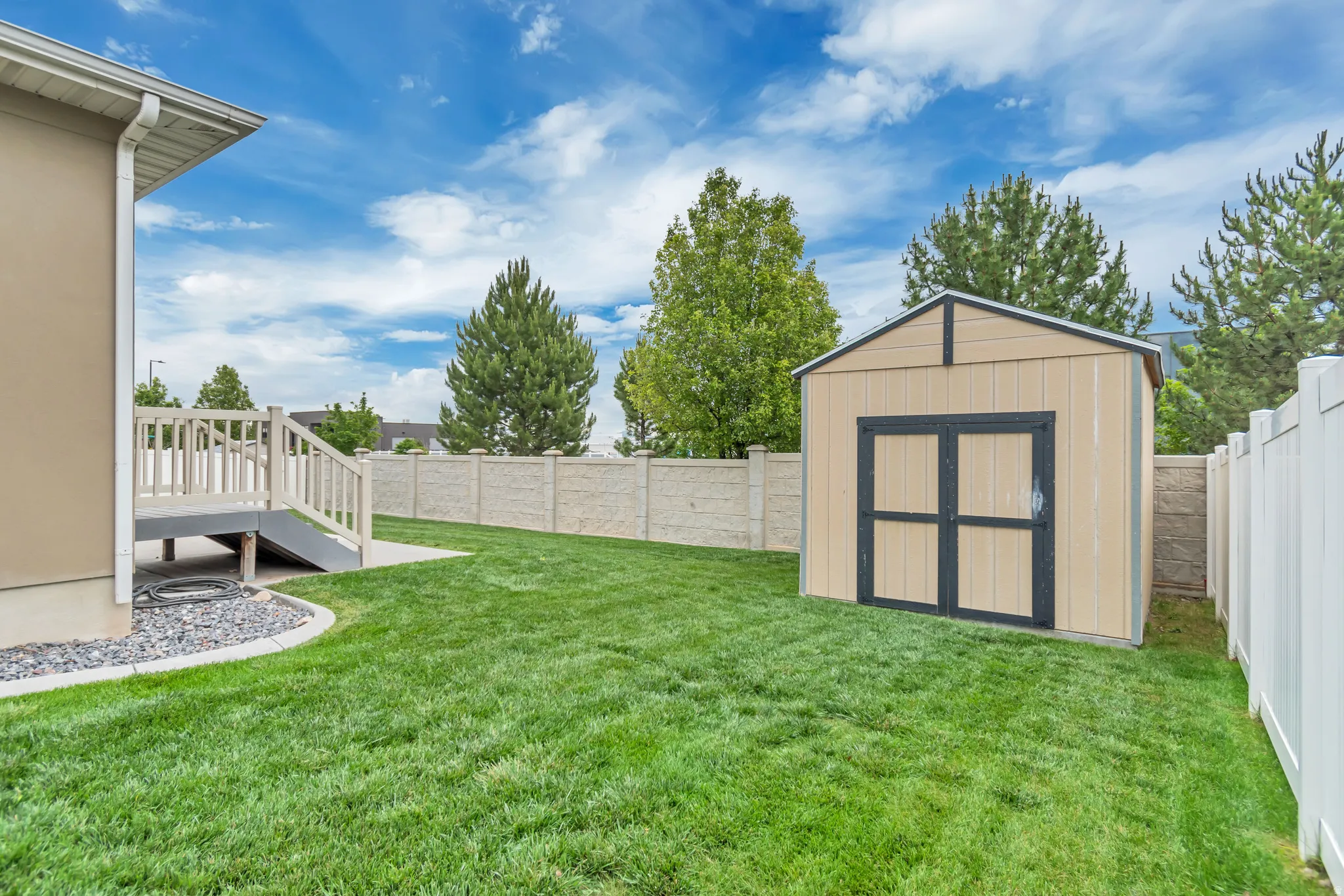 Expansive fenced backyard featuring a storage shed, concrete patio area, and a wood deck with railings