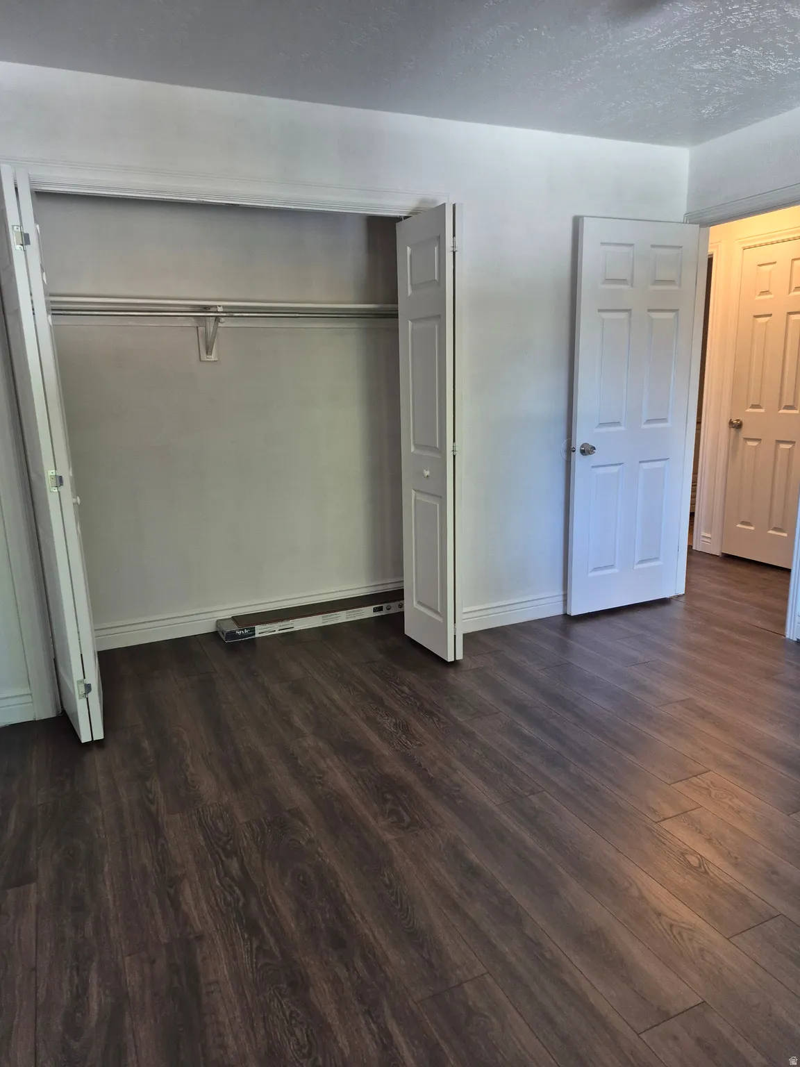 Bedroom featuring dark wood-finish flooring, white baseboards, and a bi-fold door closet with an interior hanging rod