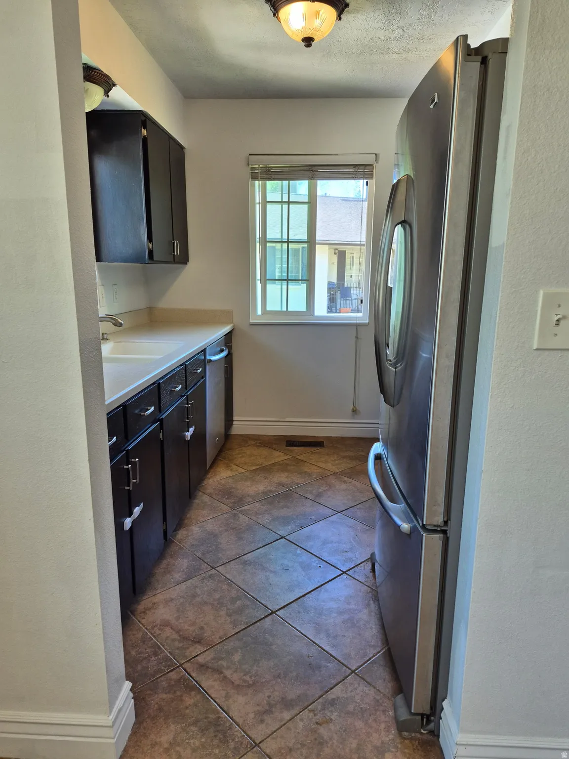 Compact kitchen featuring dark wood-finish cabinetry, light countertops, and a window with horizontal blinds