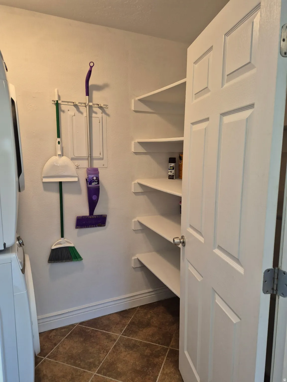 Utility area featuring a white four-panel door, multiple floating wall shelves, and brown-toned square floor tiles