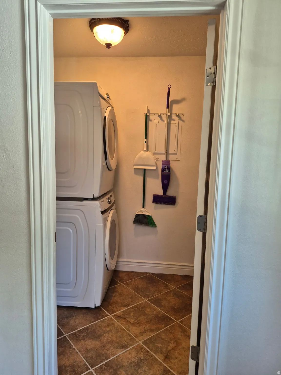 Compact laundry area featuring tile flooring, a stacked washer and dryer, and a flush mount ceiling light fixture