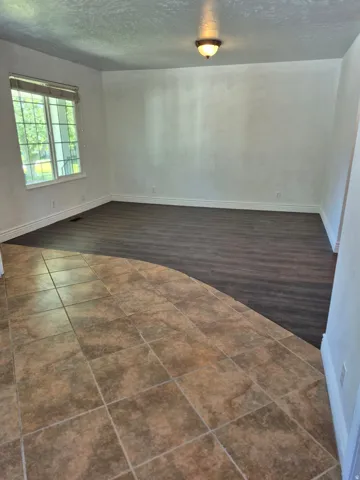 Spacious room featuring wood-finish flooring, a large window with blinds, and a semi-flush mount ceiling light