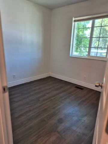 Neutral-toned room featuring wood-finish flooring, white baseboards, and a window with blinds