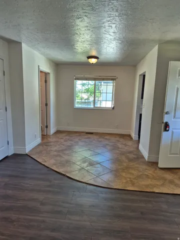 Room featuring mixed flooring with wood-finish planks and square tiles, a large window with blinds, and a flush-mount ceiling light fixture