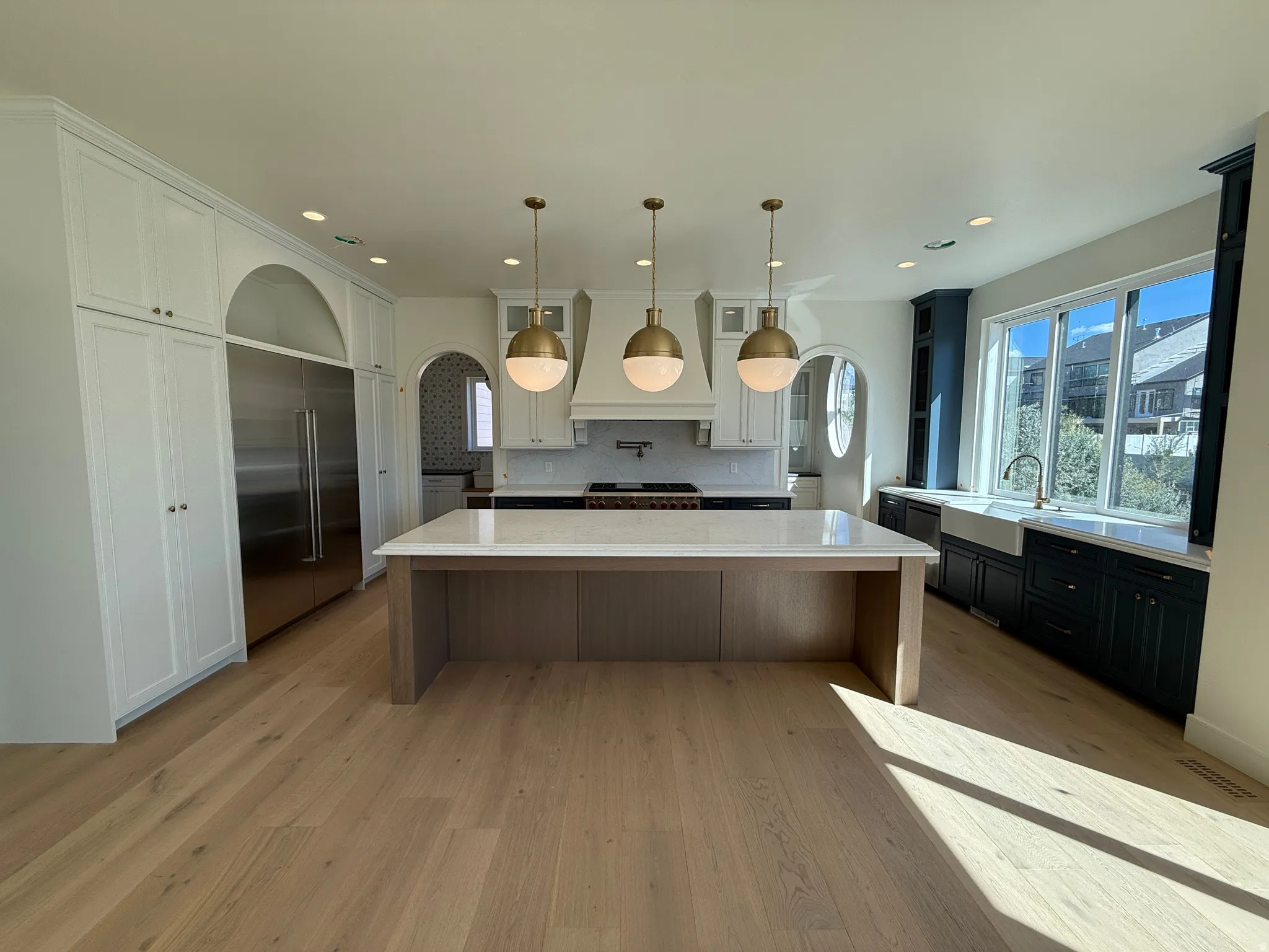 Expansive kitchen featuring a large central island with a light-toned countertop, light wood-finish flooring, and white cabinetry