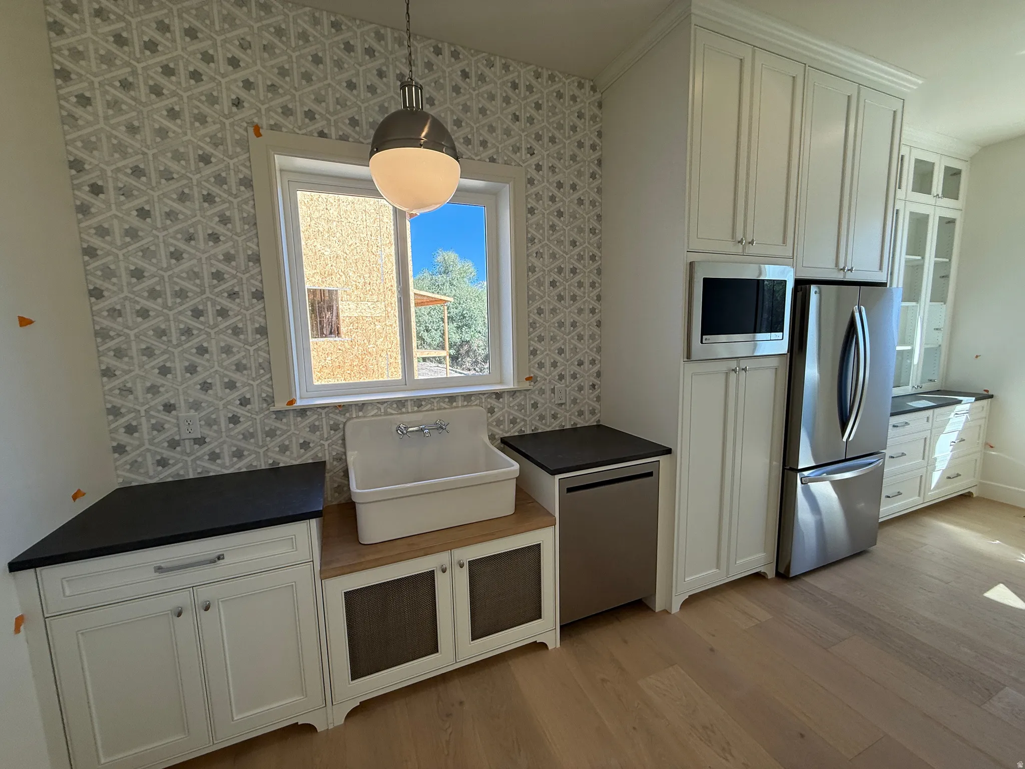 White cabinetry with dark countertops, a large utility sink, stainless steel appliances, and wood-finish flooring