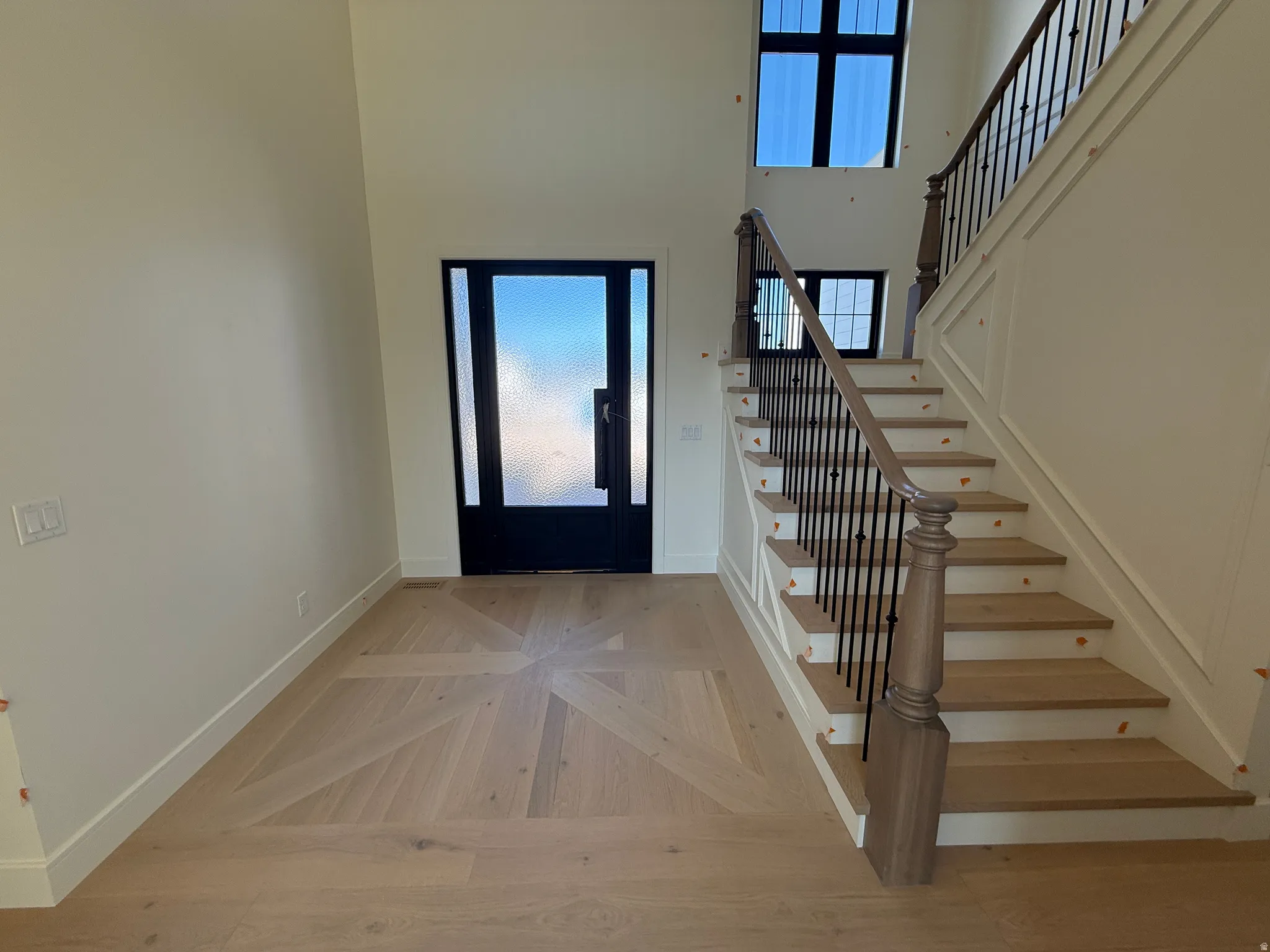 Two-story foyer with a decorative wood-finish floor inlay, grand staircase with wrought iron balusters, and transom windows
