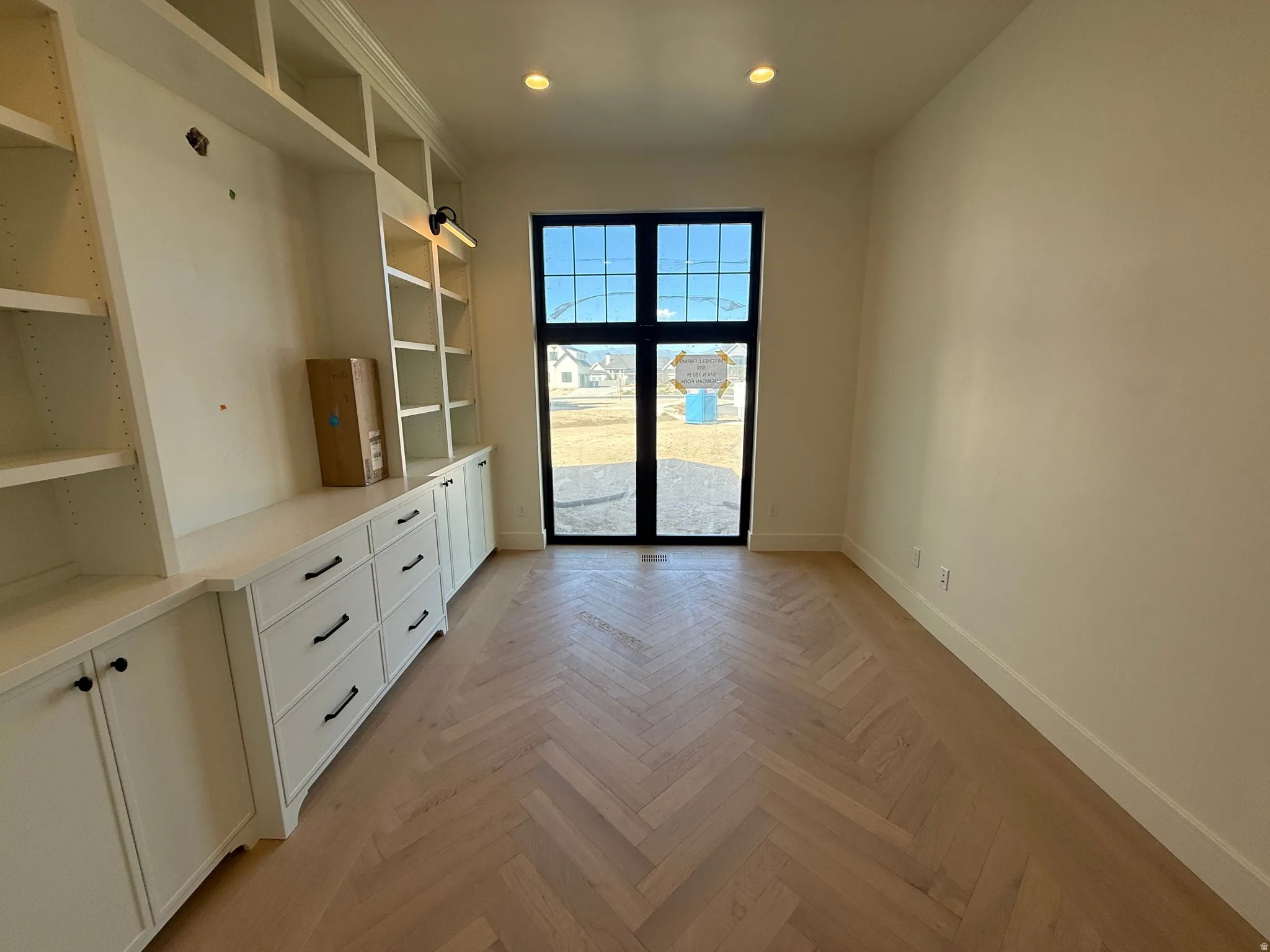 Herringbone wood-finish flooring, built-in cabinetry with black hardware, recessed lighting, and a full-light exterior door