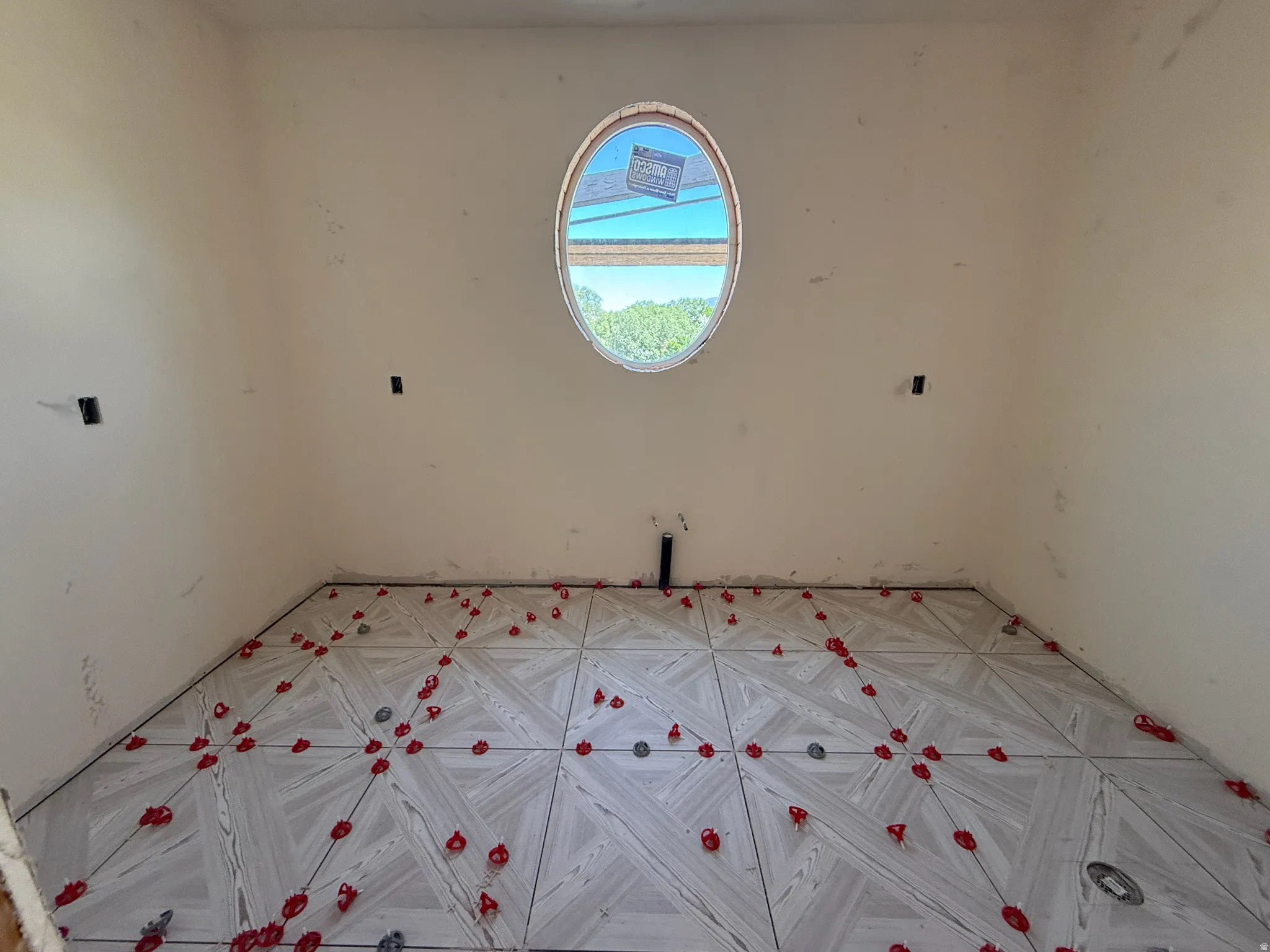 Oval window providing natural light, textured tile flooring with a geometric pattern, and wall-mounted electrical outlets