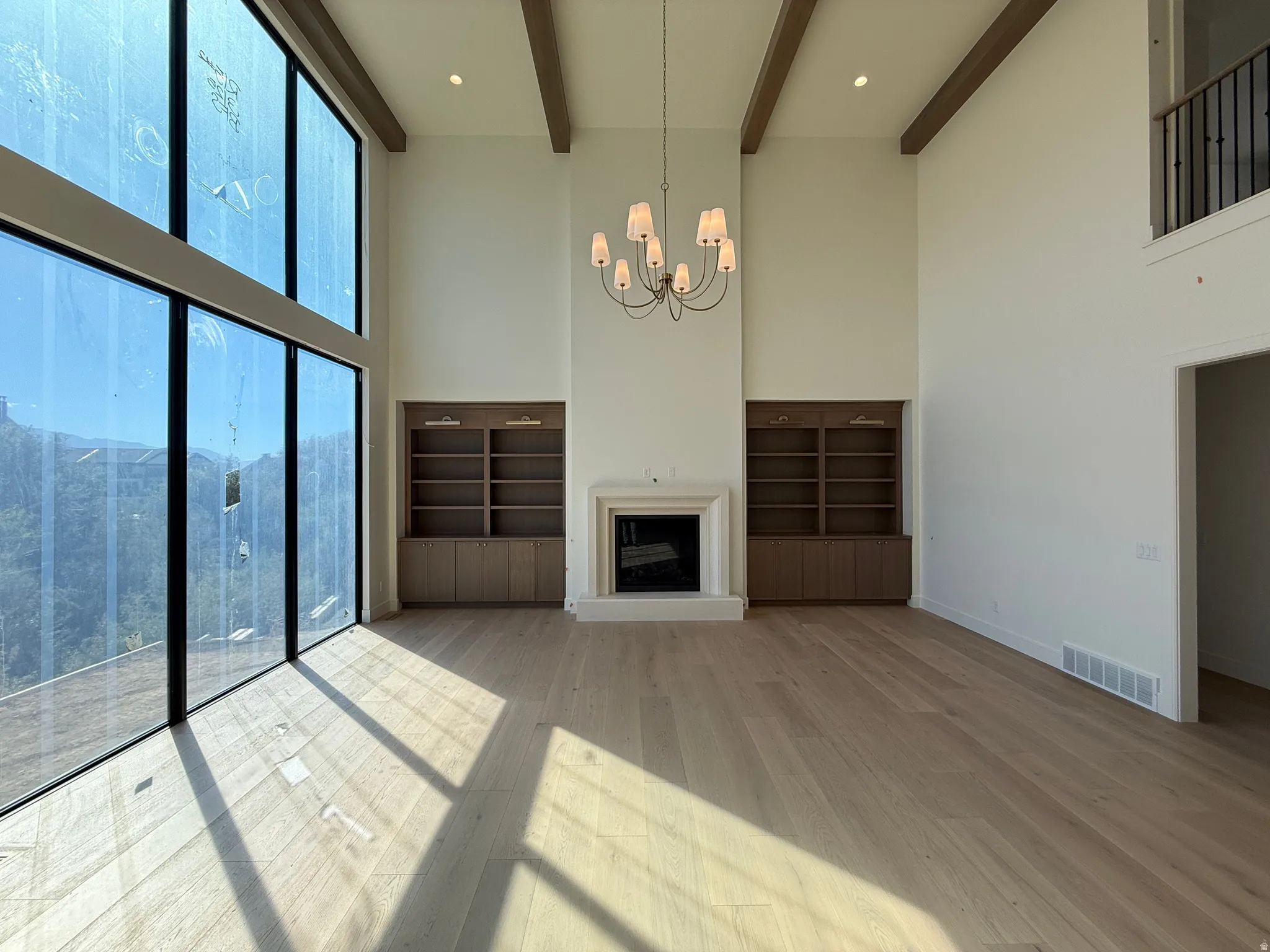 Full-height windows, wood-finish flooring, exposed ceiling beams, built-in shelving, and a prominent fireplace with a substantial mantel