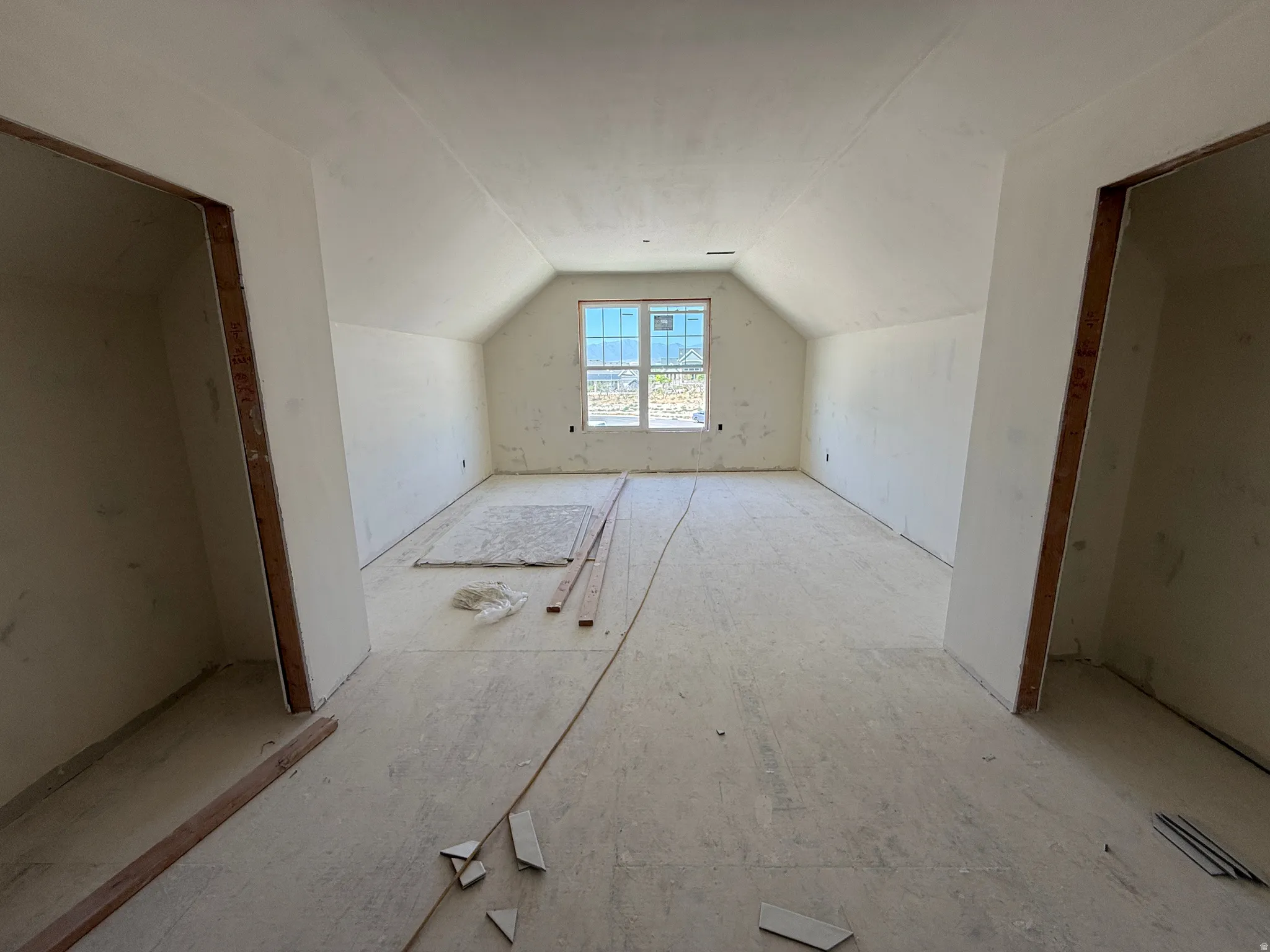 Spacious room featuring a vaulted ceiling, recessed window, and unfinished flooring