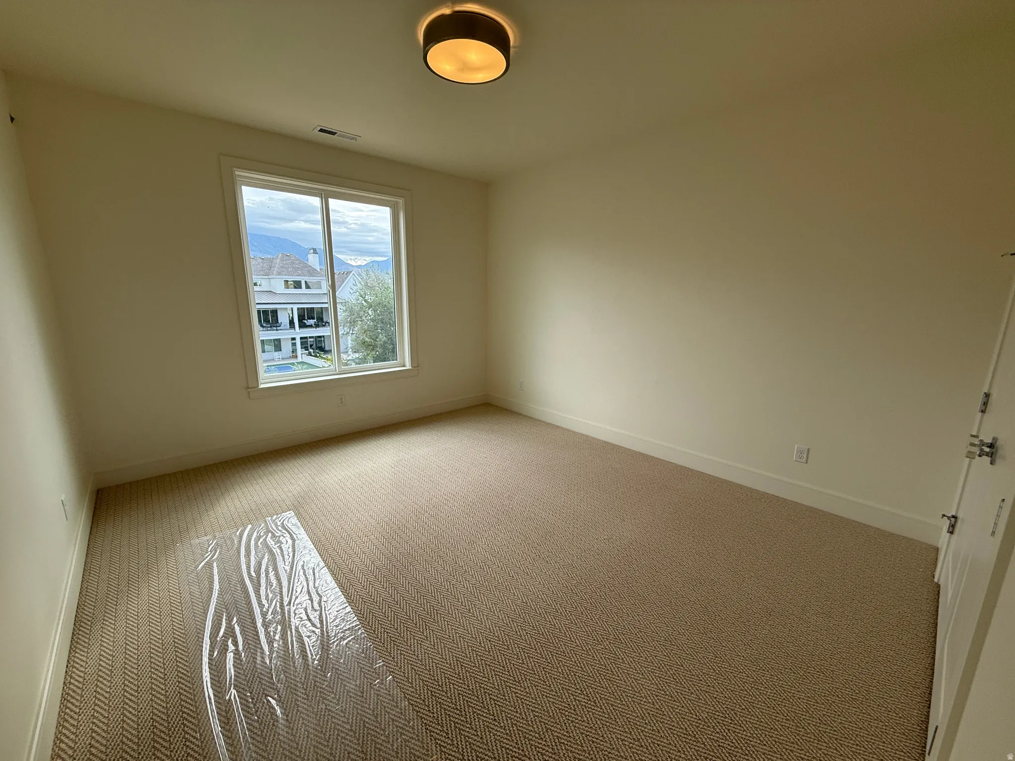 Spacious room featuring a large window, neutral wall paint, patterned carpeting, and a flush mount ceiling light