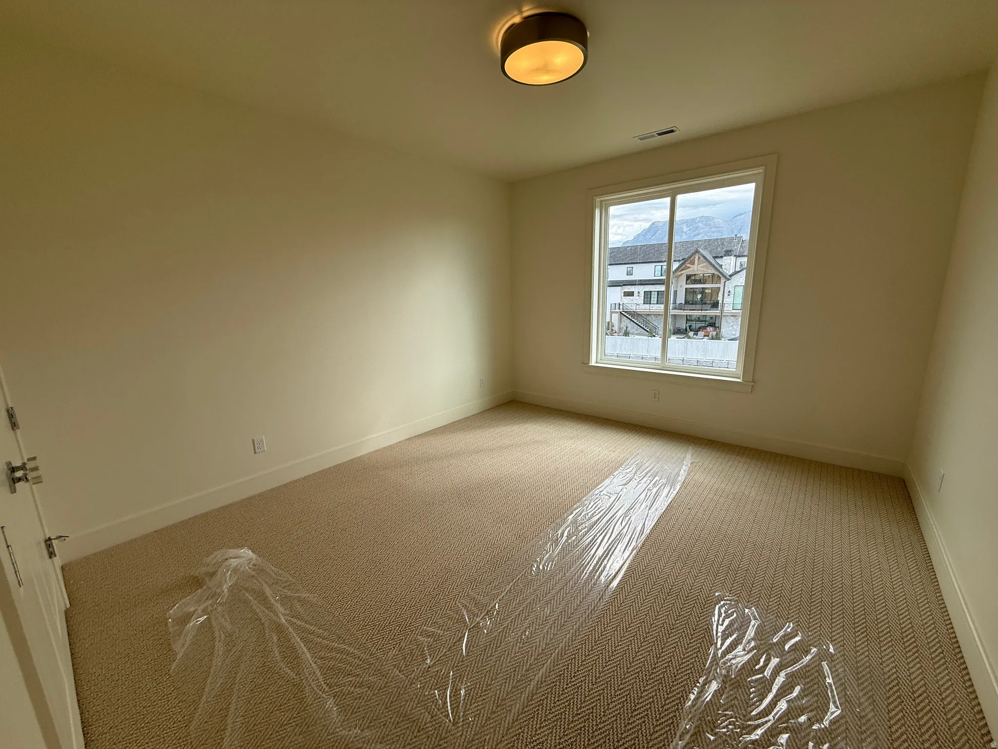 Spacious room featuring neutral wall paint, patterned carpet flooring, a large window, and a drum ceiling light fixture