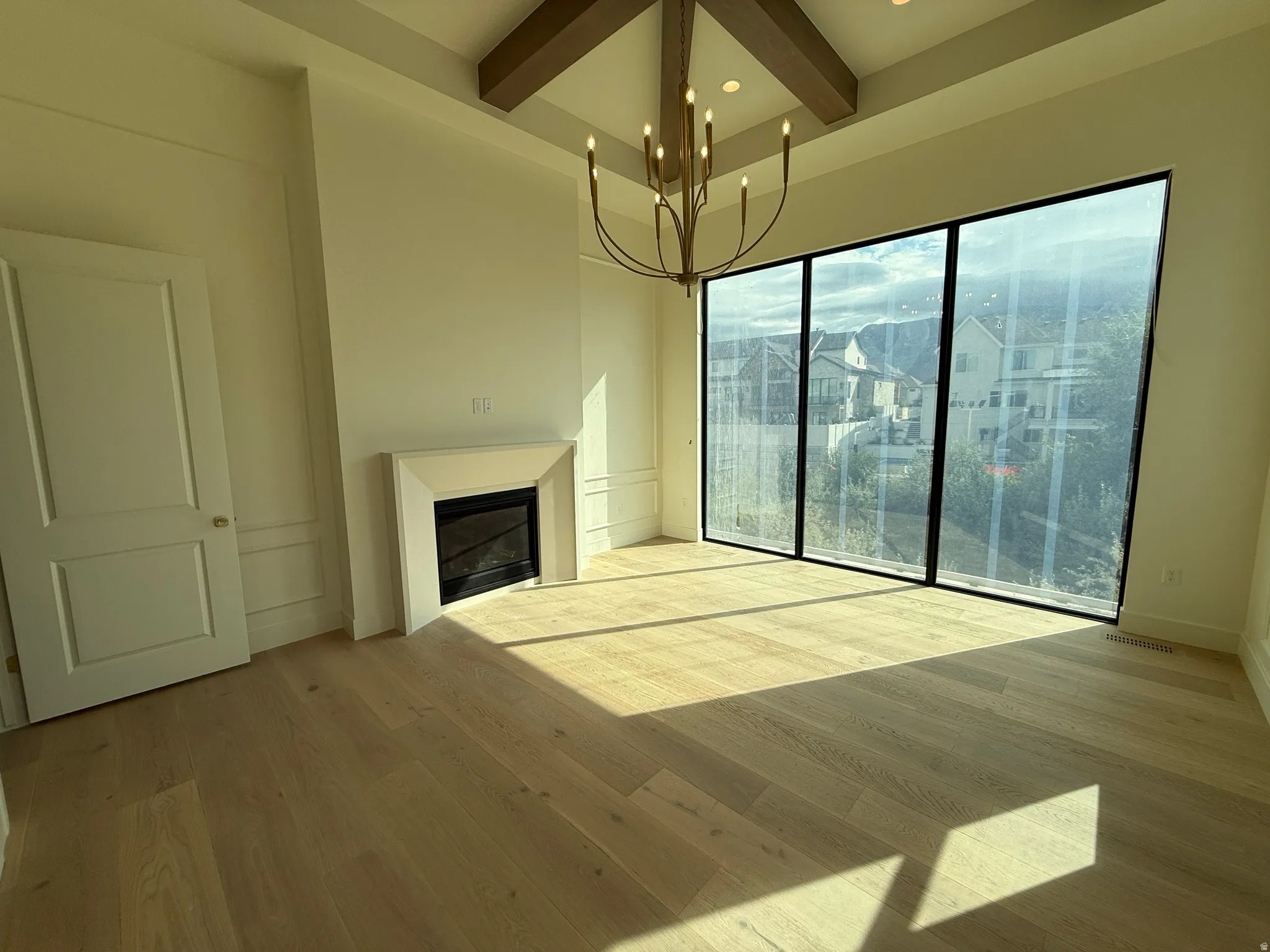 Spacious room featuring wood-finish flooring, a contemporary chandelier, a built-in fireplace with a mantel, and panel wall detailing