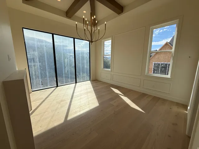 Primary Bedroom featuring Vaulted ceiling with exposed wood beams, wood-finish flooring, large multi-pane windows, decorative wall molding, and a chandelier with candelabra bulbs