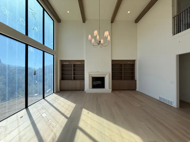 Full-height windows, wood-finish flooring, exposed ceiling beams, built-in shelving, and a prominent fireplace with a substantial mantel