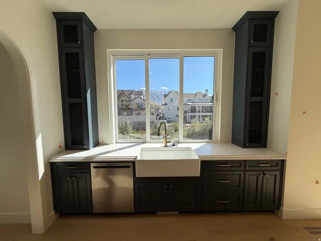 Central window with a farmhouse sink, brass-finish faucet, and integrated stainless steel dishwasher