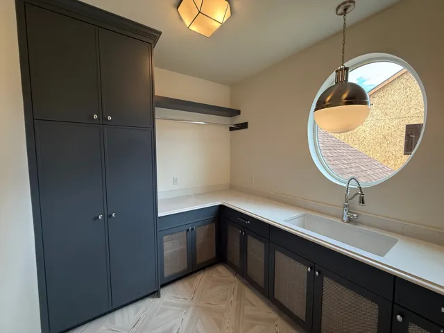 Built-in cabinetry with paneled doors, stone-finish countertops, undermount sink with gooseneck faucet, circular window, and patterned tile flooring