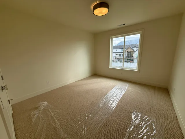 Spacious room featuring neutral wall paint, patterned carpet flooring, a large window, and a drum ceiling light fixture
