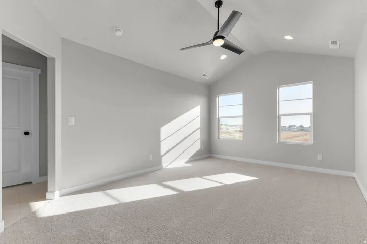 Spacious room featuring vaulted ceilings, a ceiling fan with integrated lighting, recessed lighting, two windows, and neutral carpet flooring