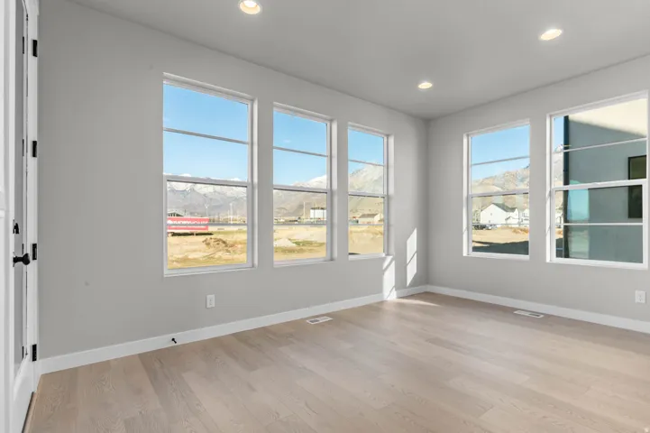 Expansive room with five large windows, light wood-finish flooring, recessed lighting, white baseboards, and a white interior door with black hardware