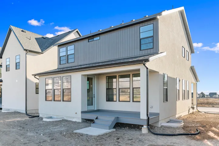 Rear exterior featuring a covered porch, multiple large windows, and a combination of stucco and vertical panel siding