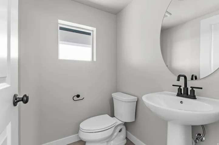 Pedestal sink with matte black faucet, wall-mounted circular mirror, and neutral wall tones