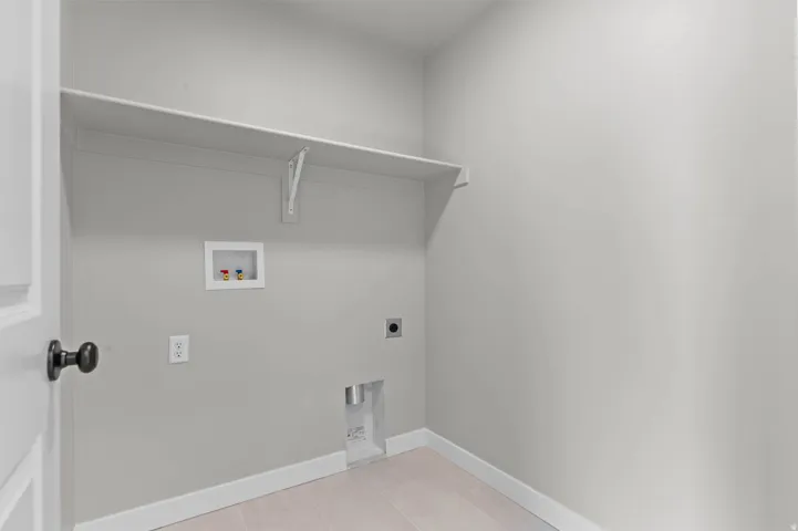 Dedicated utility space featuring a neutral color palette, integrated wall shelving, electrical outlets, and plumbing connections