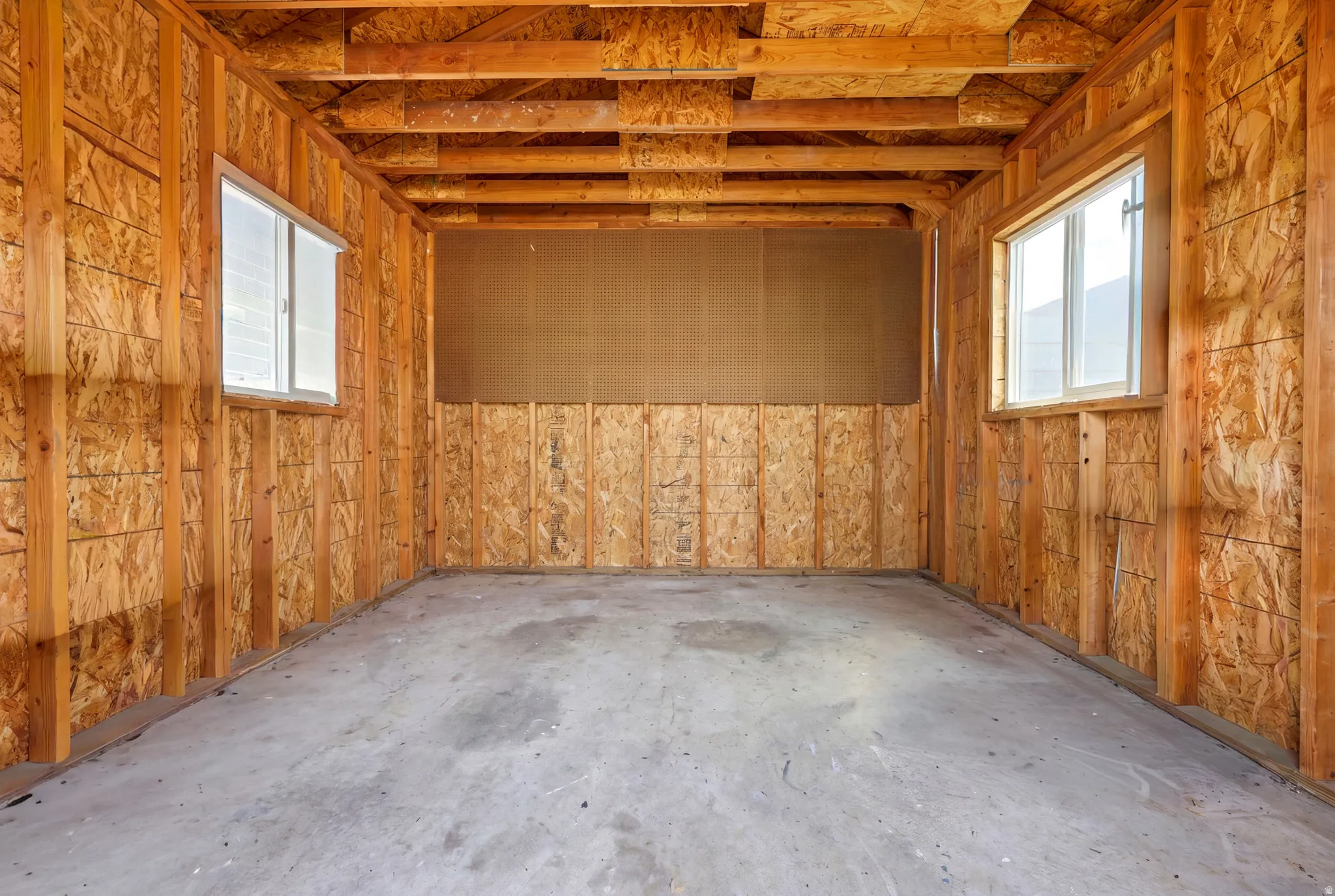 Unfinished interior space featuring exposed wood framing, oriented strand board paneling, a concrete floor, and two windows with white frames