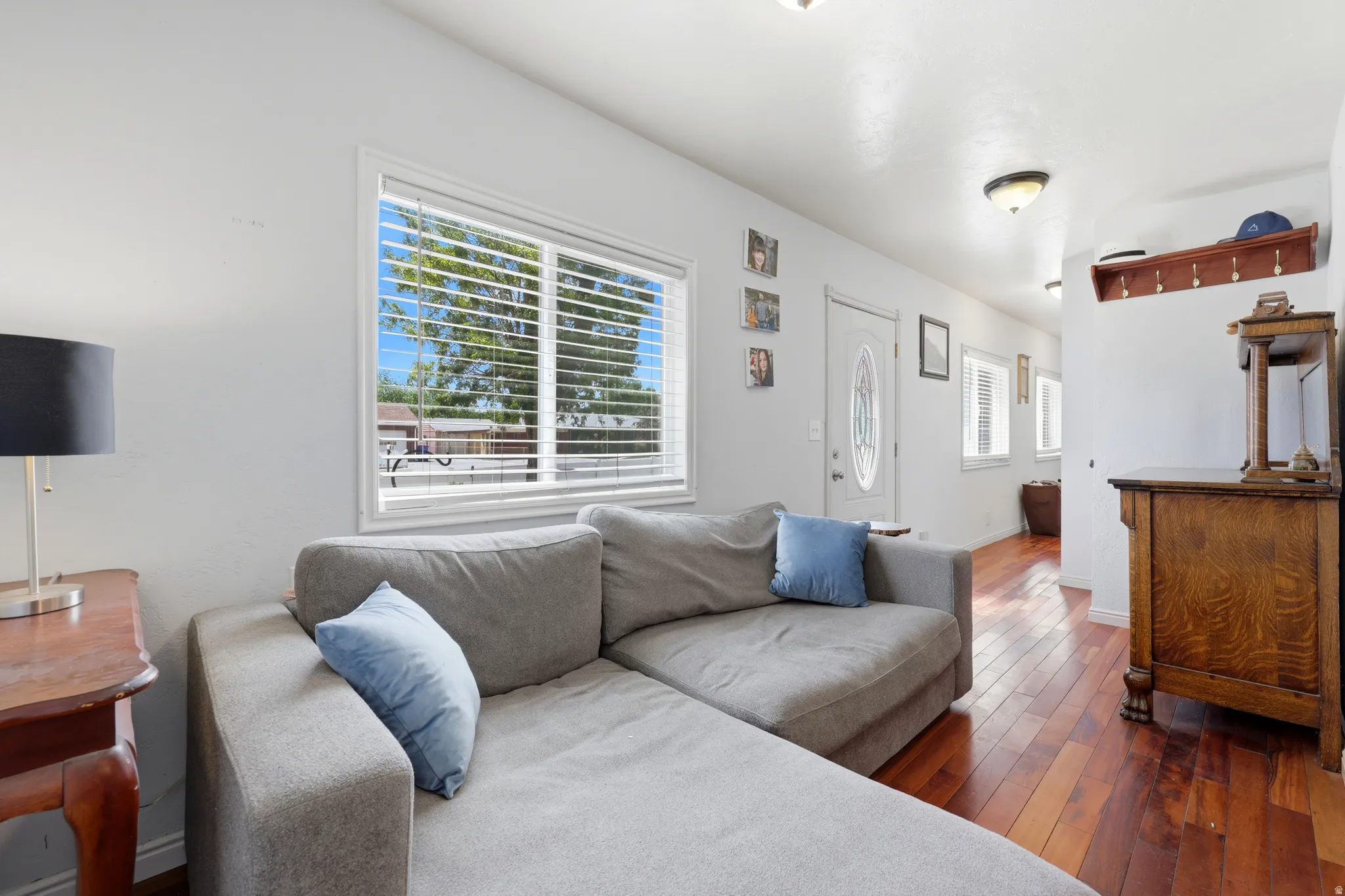 Living area featuring wood-finish flooring, white walls, and a large window with horizontal blinds
