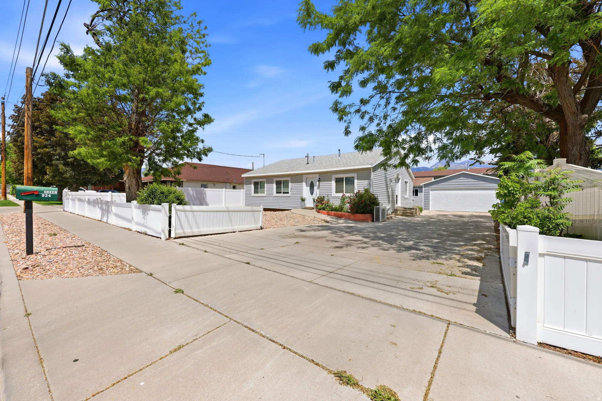 Grey siding exterior with white trim, a detached two-car garage, and a white vinyl fence