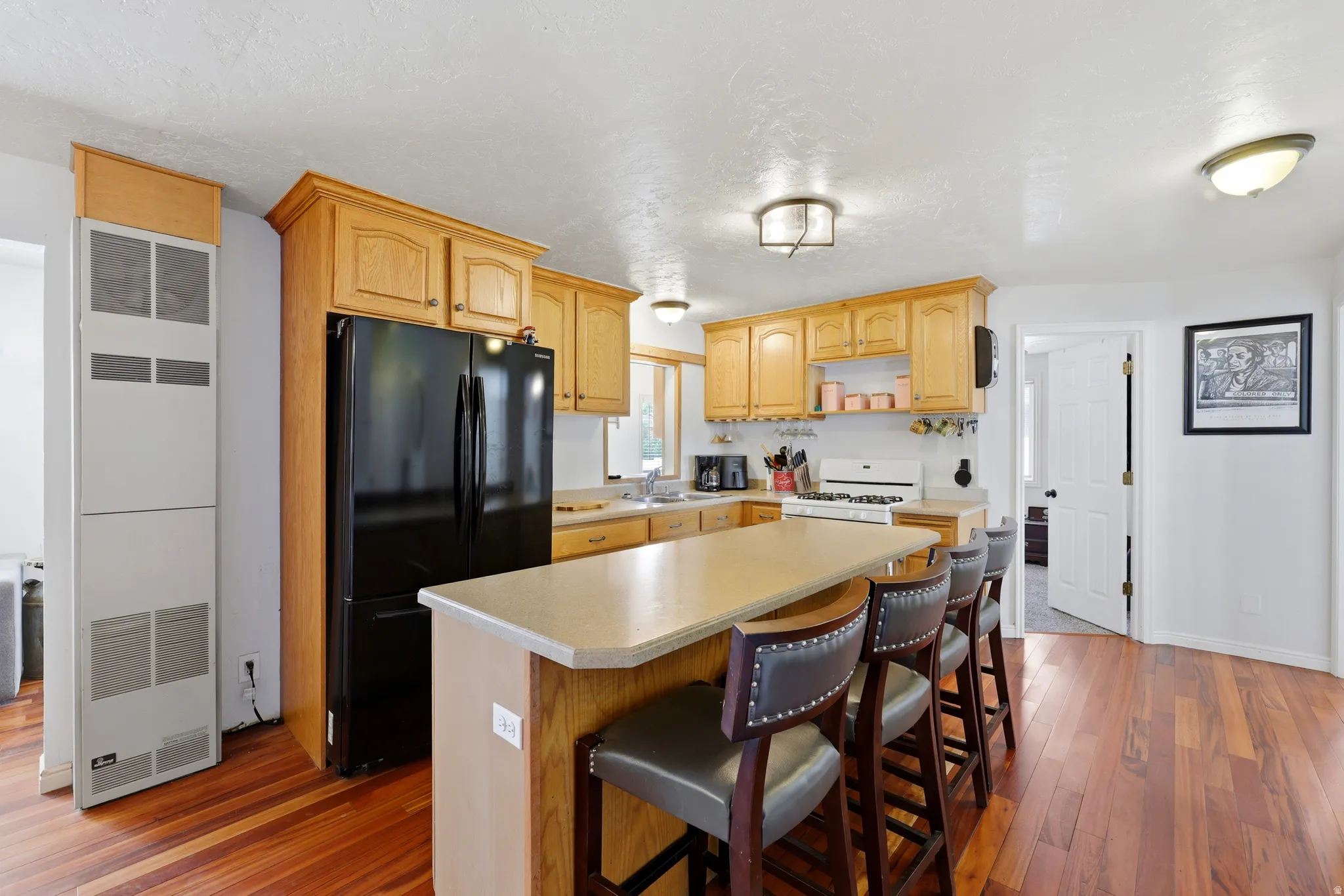 Kitchen featuring wood-finish flooring, a central island with countertop seating, light wood cabinetry, and a black French door refrigerator