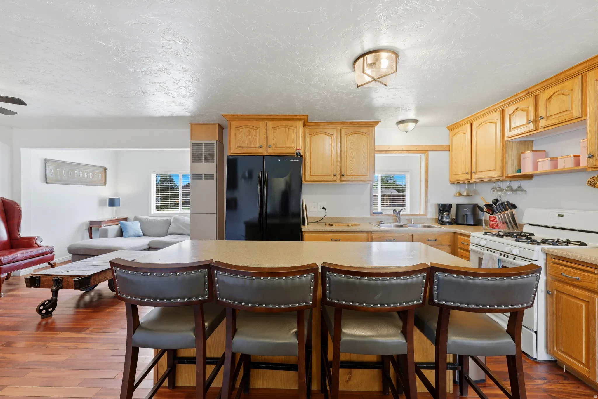 Kitchen island with integrated breakfast bar, light wood-finish cabinetry, black refrigerator, white gas range, and recessed sink