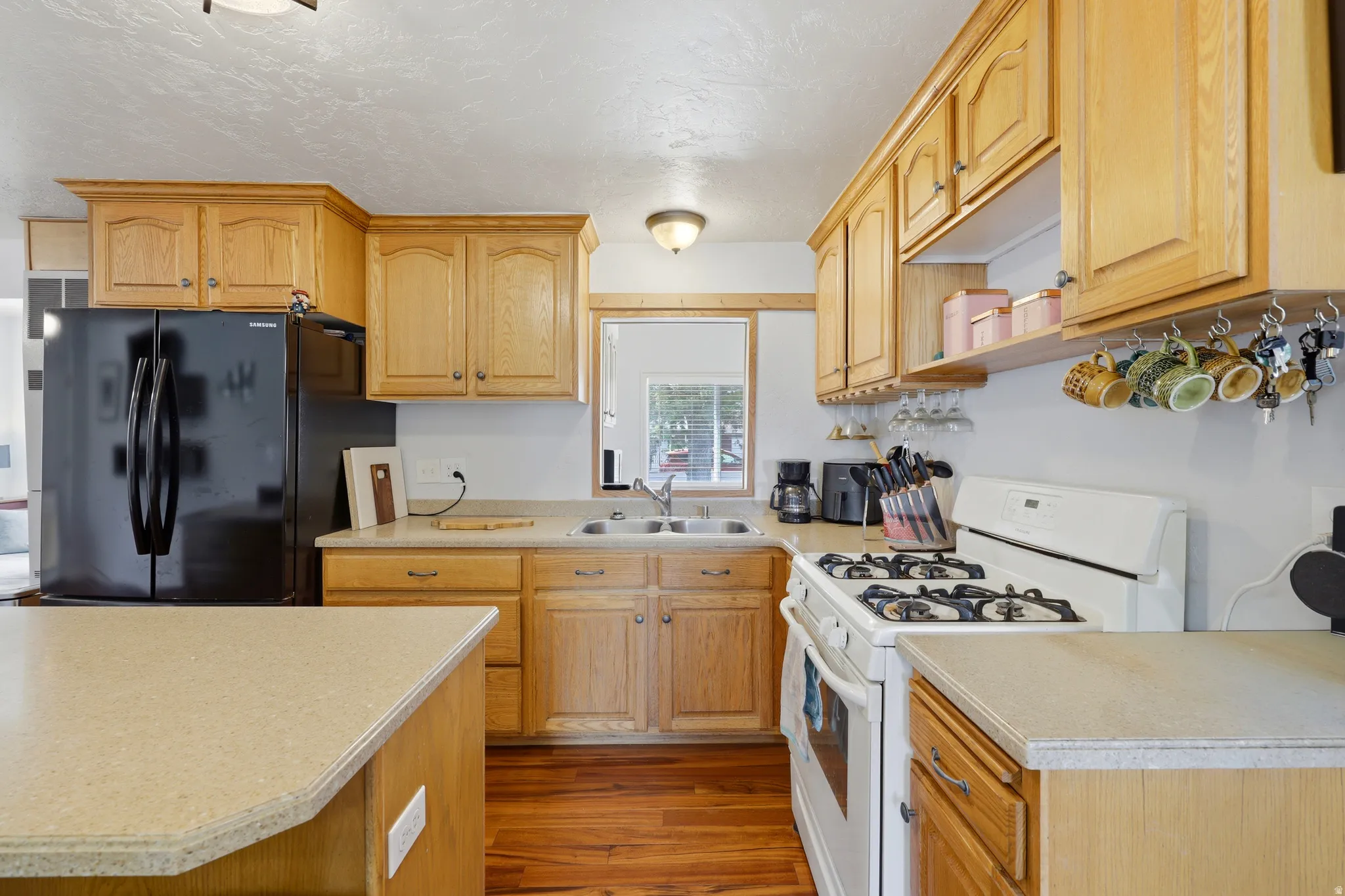 Kitchen featuring wood cabinetry, light-toned countertops, a black refrigerator, and a white gas range