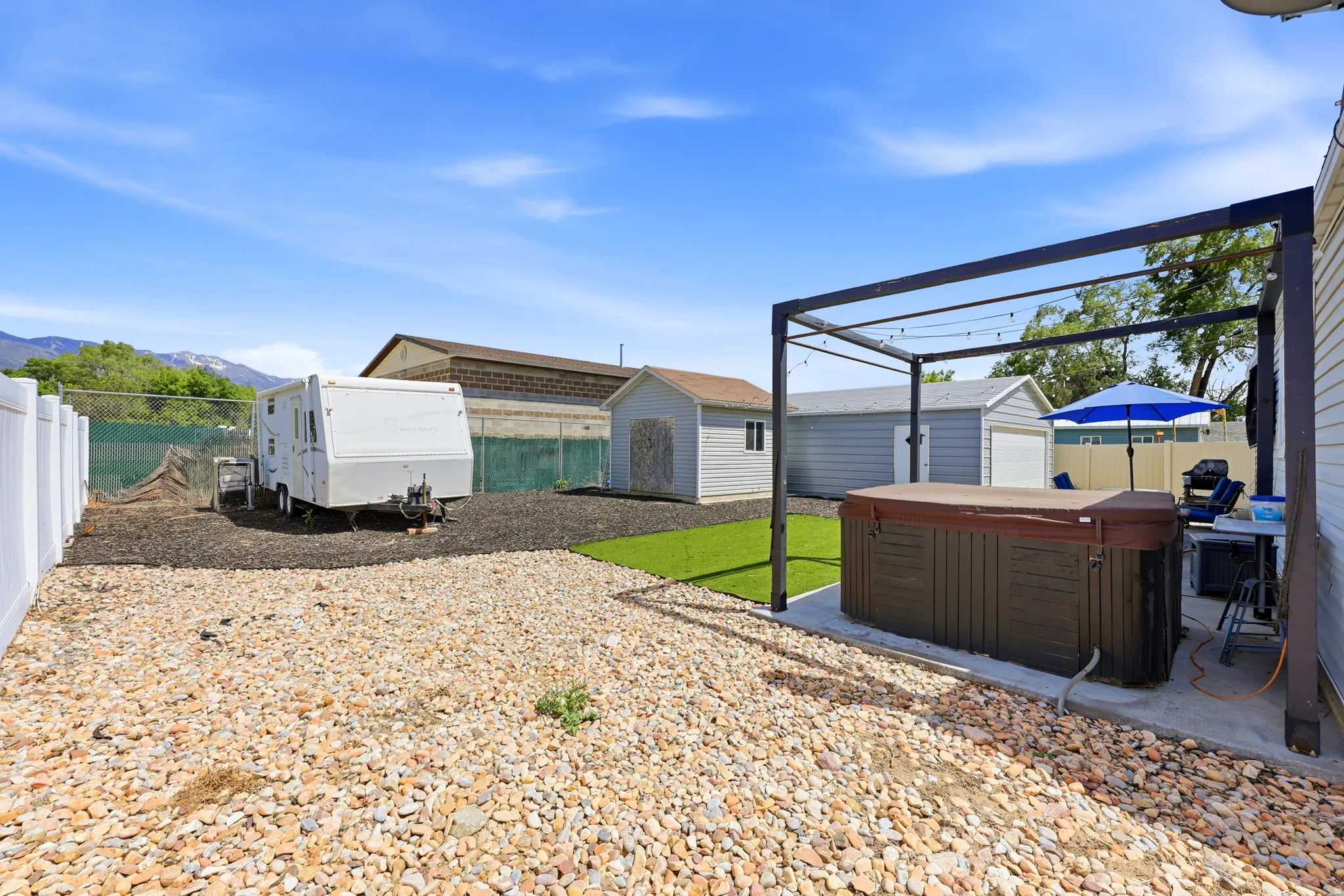 Expansive backyard featuring a hot tub under a pergola, artificial turf, and a gravel-covered area