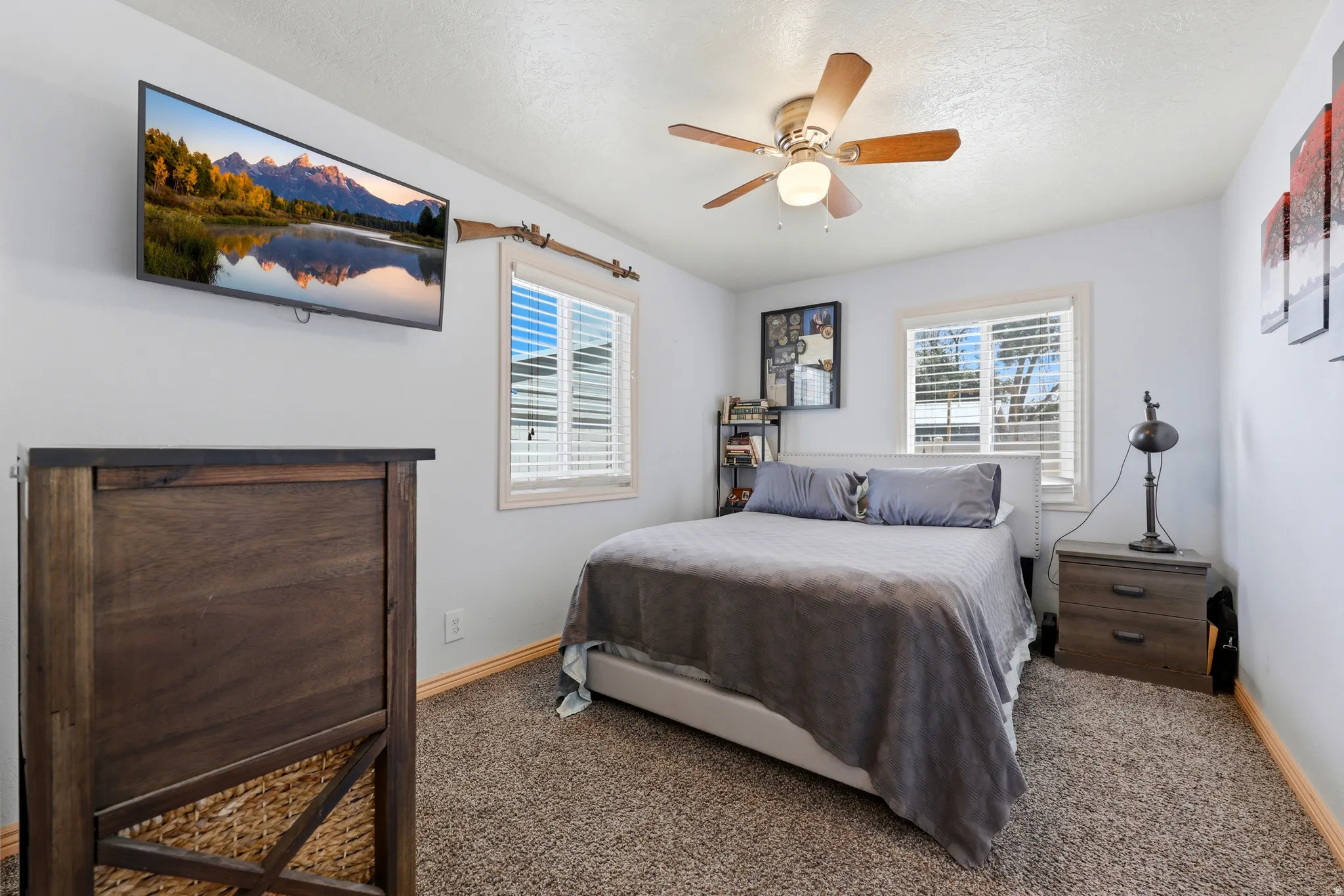 Carpeted room featuring a ceiling fan with integrated lighting, two windows with blinds, and white painted walls