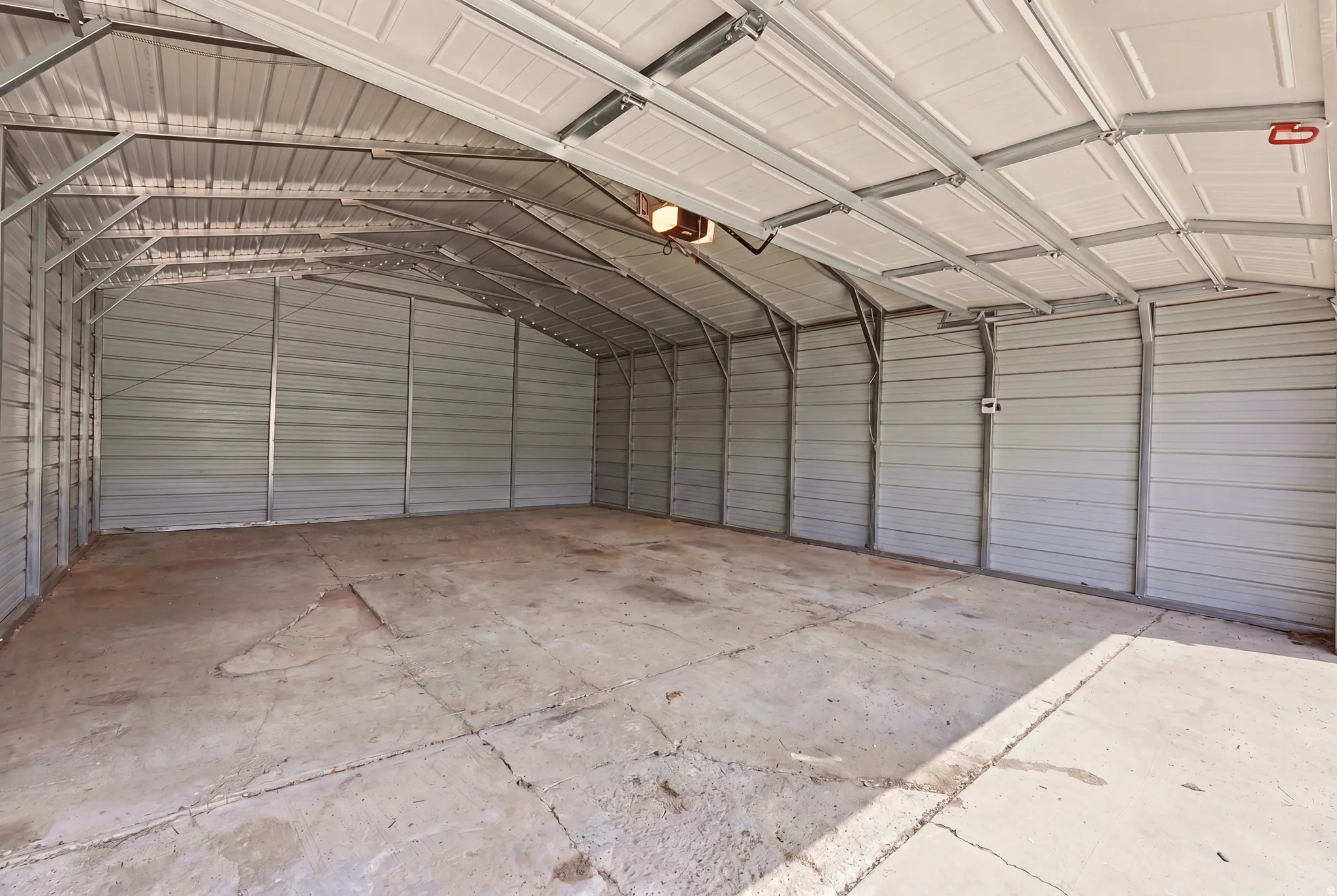 Spacious metal carport with a concrete slab floor, corrugated metal walls, and an overhead garage door