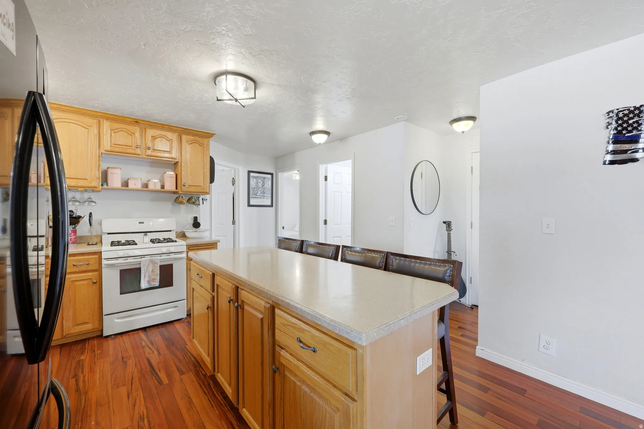 Kitchen featuring wood-finish flooring, a central island with countertop seating, light wood cabinetry, white appliances, and recessed lighting