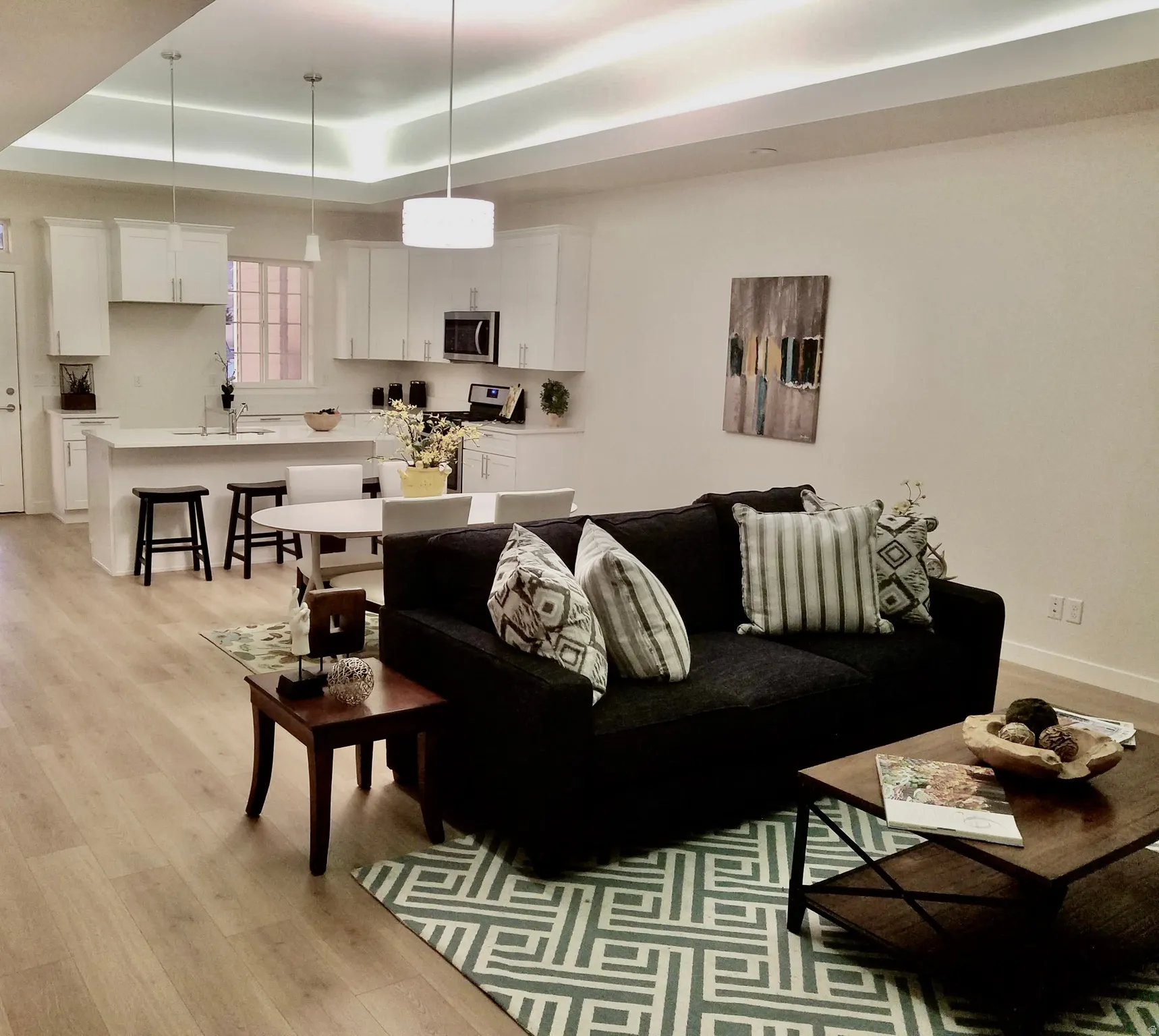Open-concept living space featuring wood-finish flooring, recessed ceiling lighting, and a kitchen with white cabinetry, a center island with bar seating, and stainless steel appliances