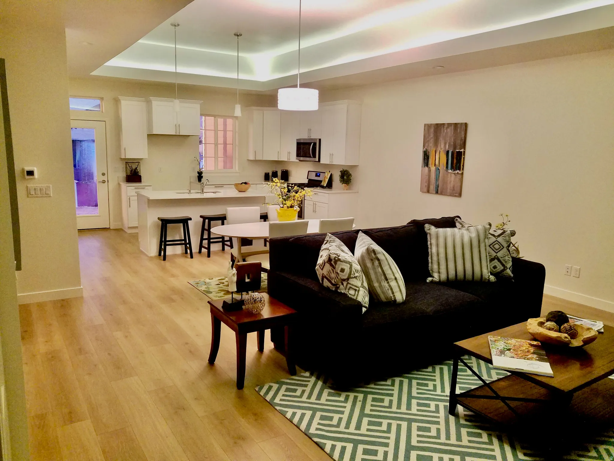 Open-concept living area with wood-finish flooring, recessed lighting, and a tray ceiling