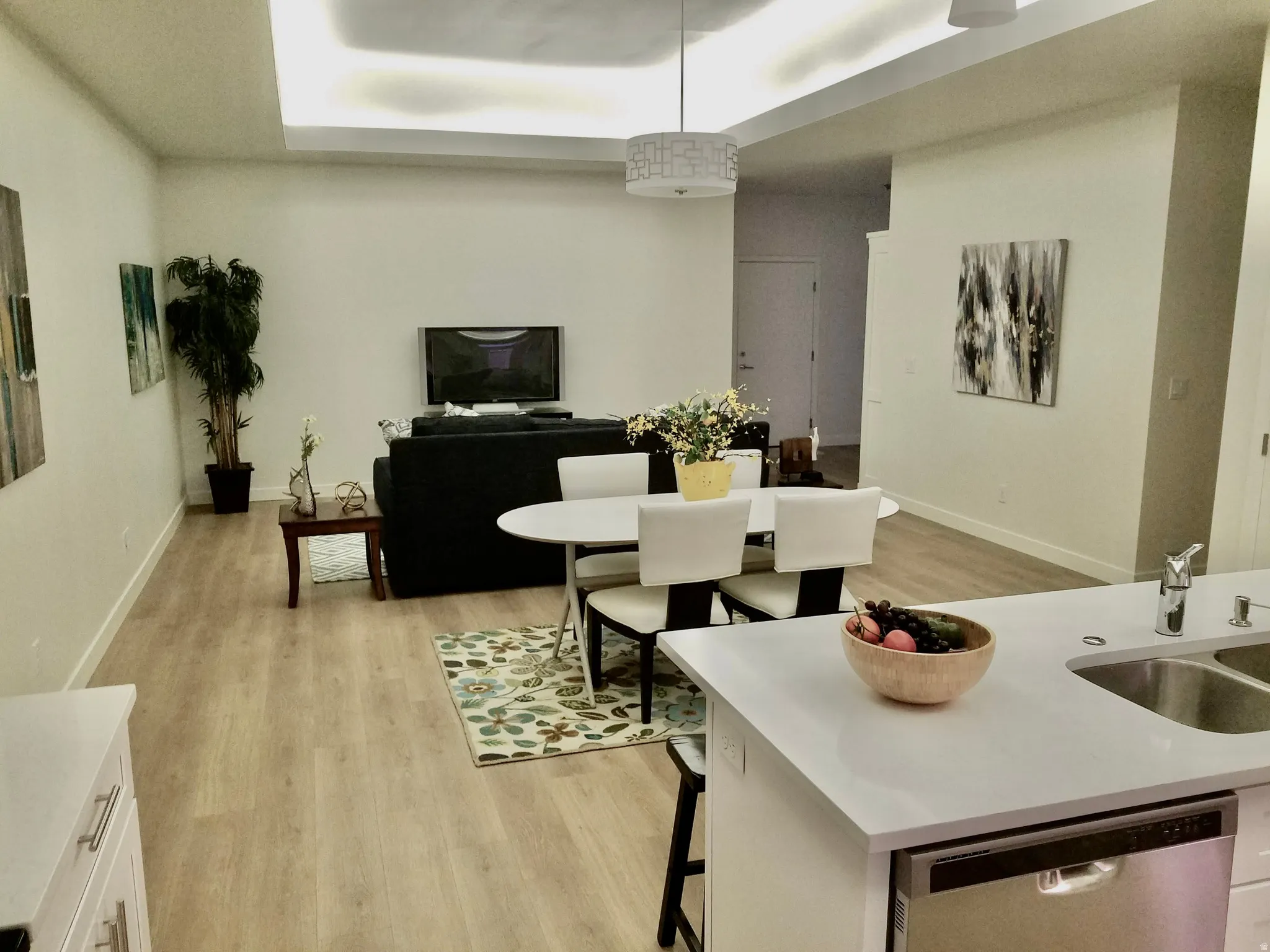 Open-concept living space featuring wood-finish flooring, recessed tray ceiling lighting, and an integrated kitchen island with a stainless steel sink and dishwasher