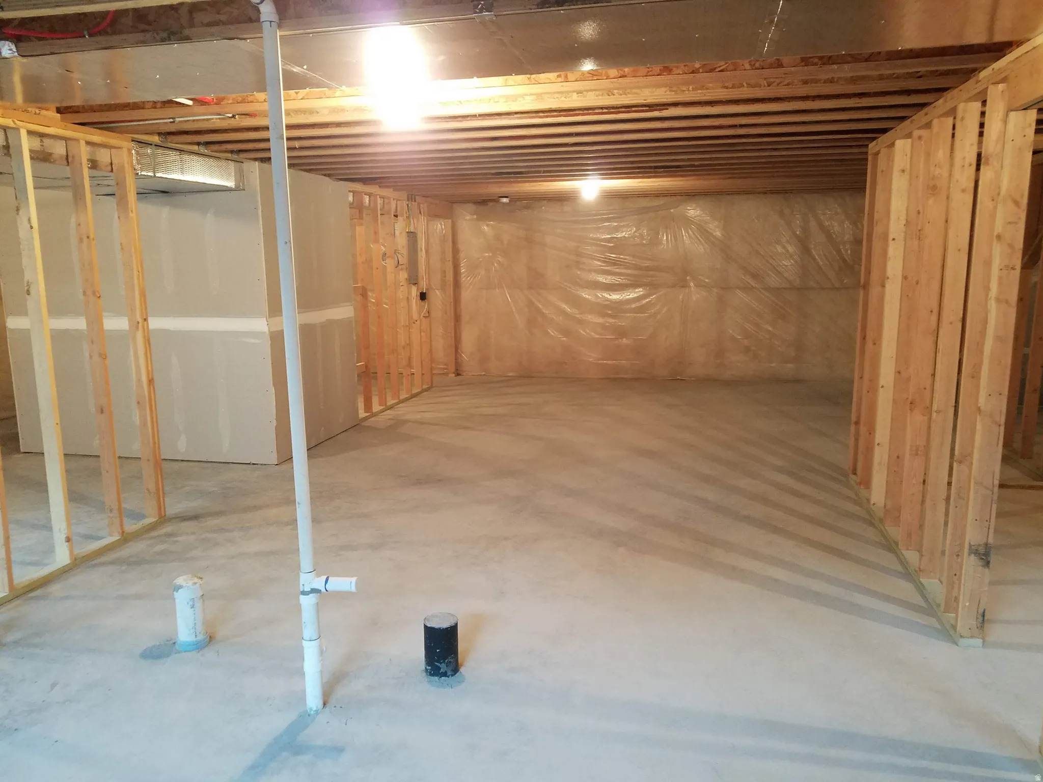 Unfinished basement with concrete flooring, exposed wood ceiling joists, and partial wood framing for future development