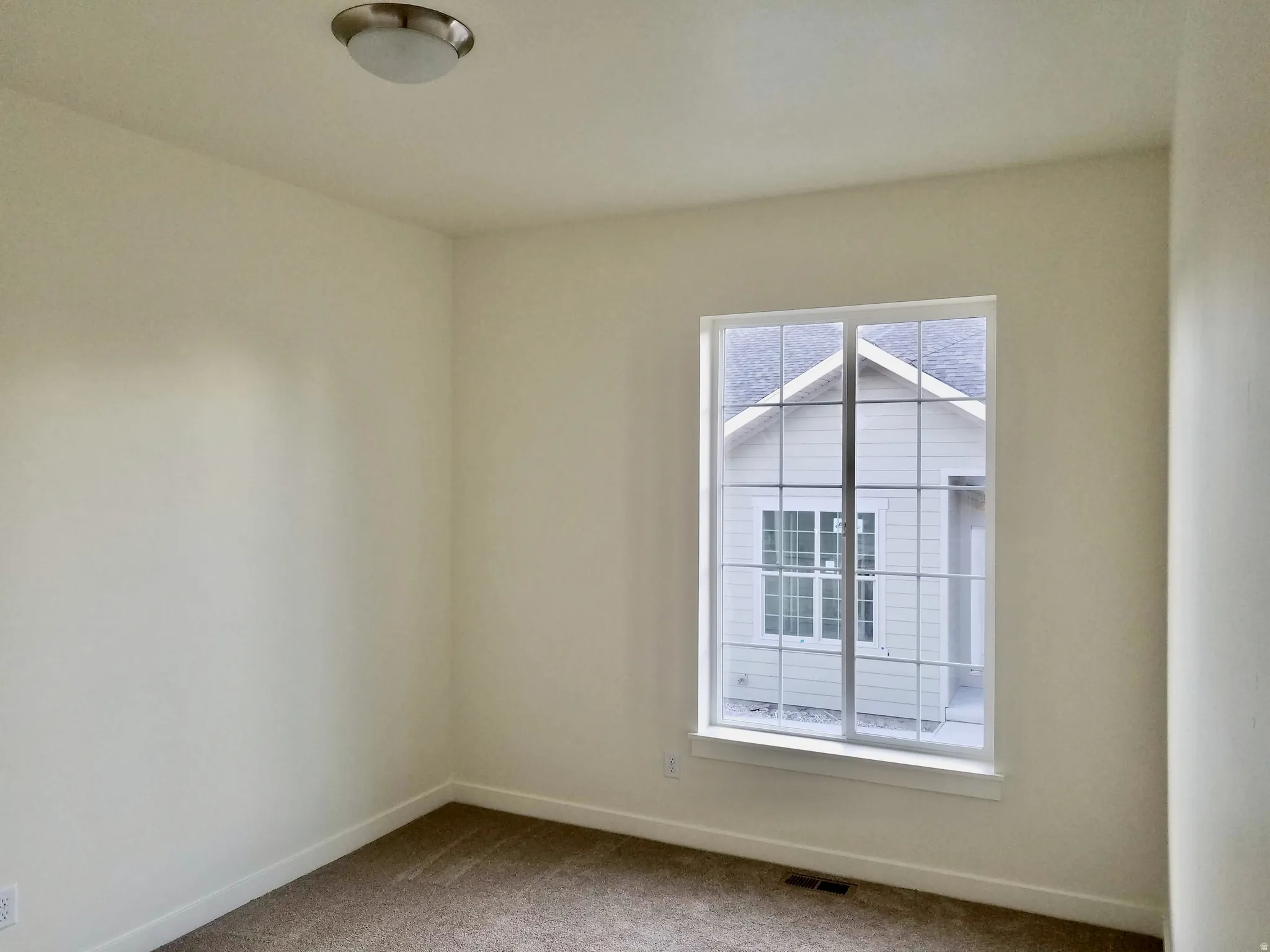 Room featuring light neutral wall paint, a single window with white trim, brown carpet, and a flush-mount ceiling light fixture