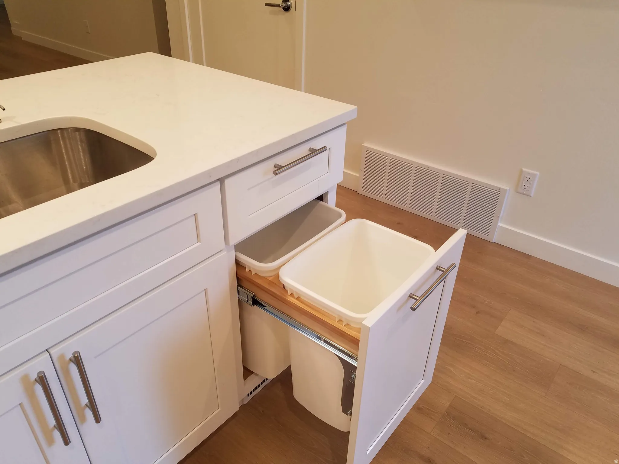 Kitchen island featuring a stainless steel sink, solid surface countertop, white shaker cabinetry.