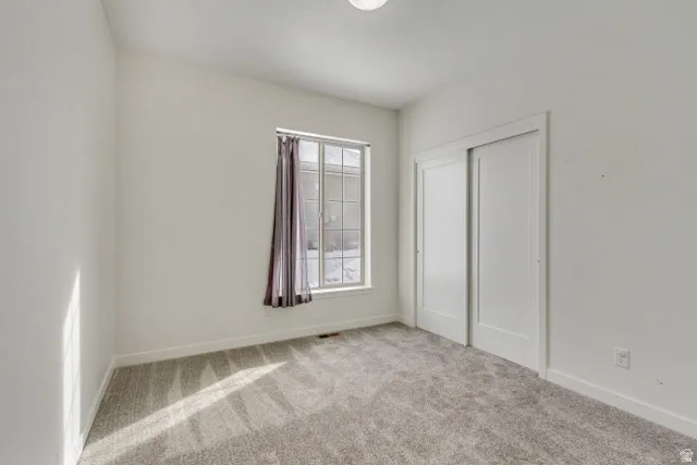 Bright interior room featuring a large window, light gray carpet, white walls, and a sliding two-panel closet door