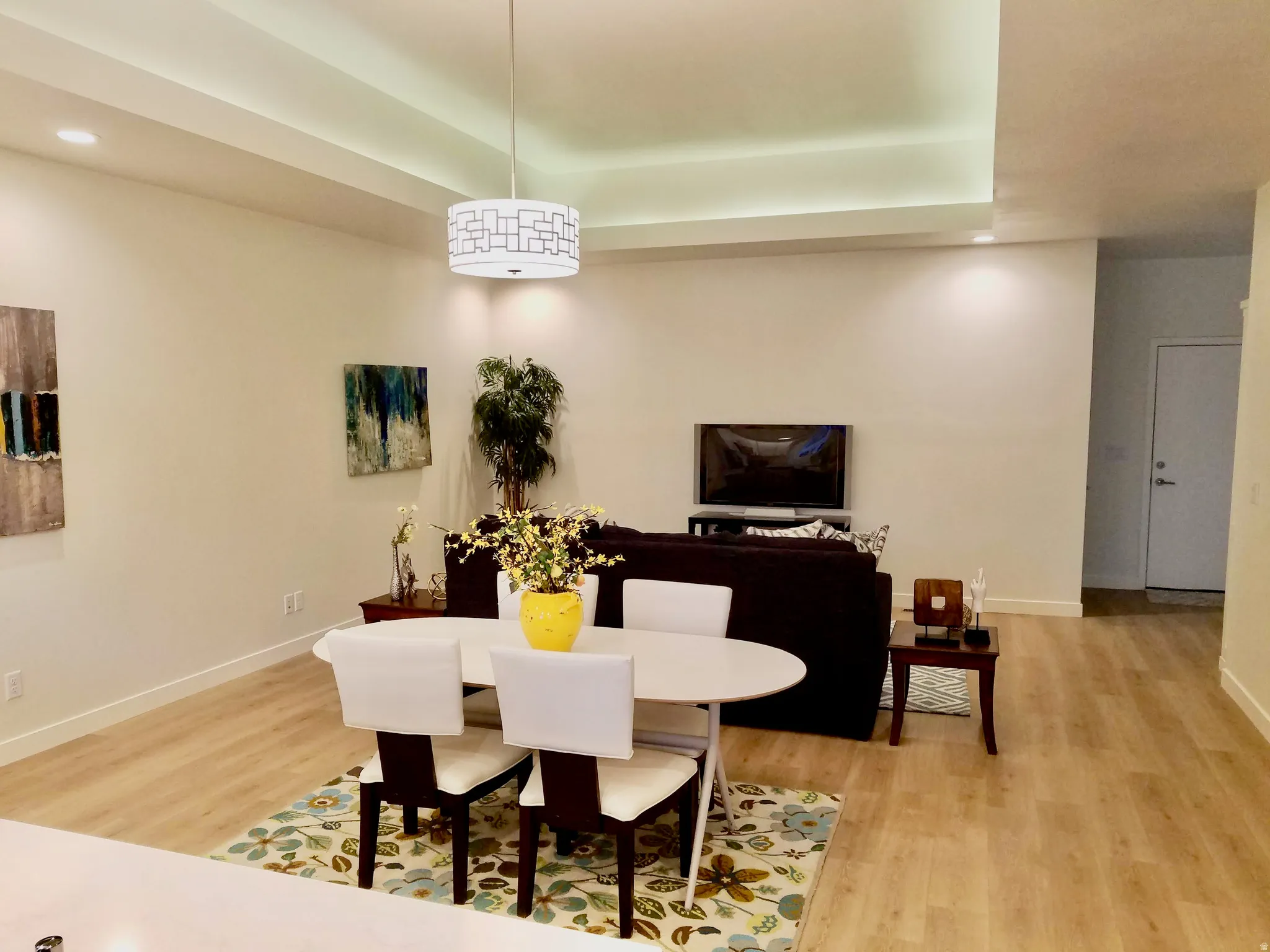 Open-concept living area featuring a decorative pendant light, recessed lighting, wood-finish flooring, a tray ceiling, and a white interior door